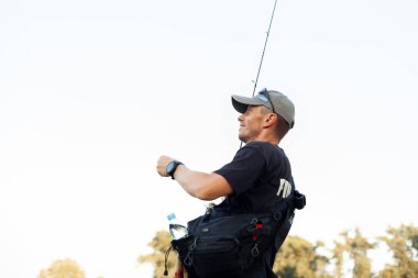 Genç gülen adam gün batımında göle olta atıyor.