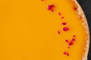 Koyu mermer arka planda, kırmızı donmuş ahududu kırıntılarıyla süslenmiş sarı mango aromalı düz peynirli kek. Desenli arkaplan