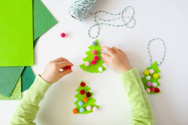 Beyaz masaüstünde Noel süsleri yapan bir çocuk. Tepeden. Düz yatıyordu. Kumaştan yapılmış el yapımı Noel ağacı.