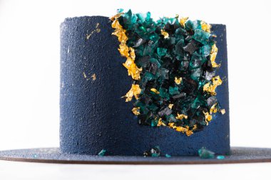 Mavi kadife kaplamayla kaplanmış ve beyaz arka planda altın yapraklarla süslenmiş lüks kremalı pasta. Sığ alan derinliği