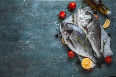 Limon dilimli taze dorado balığı, domates, jilet ve koyu mermer arka planda baharatlar. Dümdüz uzanmış balık pişmeye hazır.