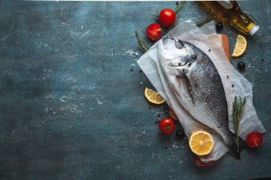 Limon dilimli taze dorado balığı, domates, jilet ve koyu mermer arka planda baharatlar. Dümdüz uzanmış balık pişmeye hazır.