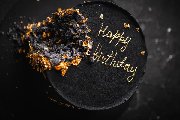 黒の高級ムースケーキはベルベットのコーティングで覆われ 暗い背景に黄金の花びらで飾られています フィールドの浅い深さ ケーキの上の幸せな誕生日のテキスト — ストック写真