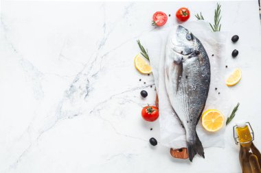 Limon dilimli taze dorado balığı, domates, jilet ve beyaz mermer arka planda baharatlar. Düz balık pişmeye hazır.