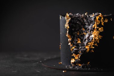 Kadife kaplamayla kaplanmış ve arka planda altın taç yapraklarıyla süslenmiş siyah lüks kremalı pasta. Sığ alan derinliği