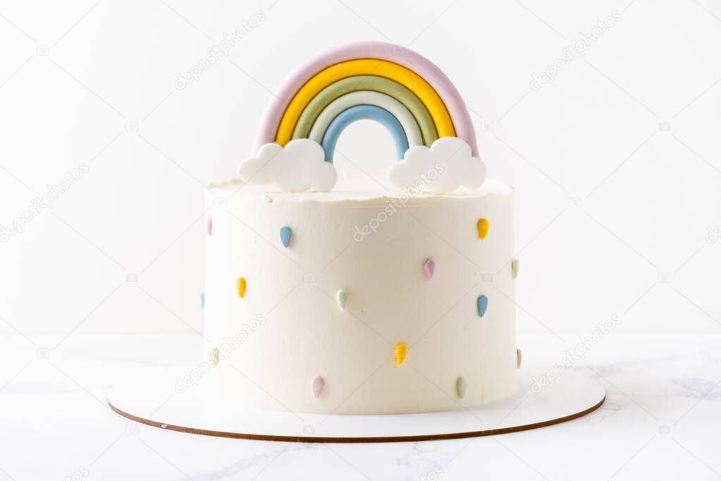 Birthday cake with white cream cheese frosting decorated with colorful mastic rainbow on the white background