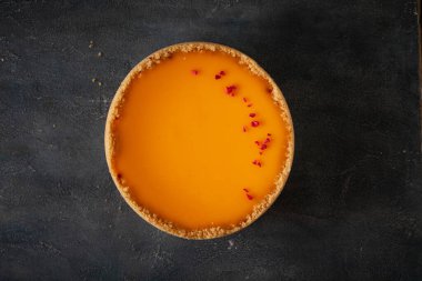 Koyu mermer arka planda, kırmızı donmuş ahududu kırıntılarıyla süslenmiş sarı mango aromalı düz bir cheesecake..