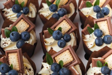 Çırpılmış krem şantili, üstü yaban mersinli ve çikolatalı kurabiyelerle süslenmiş çikolatalı kekler.