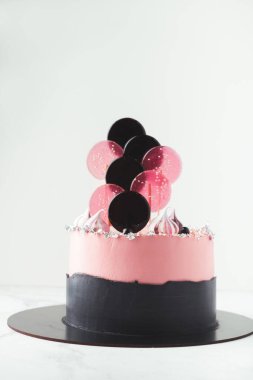 Üstünde pembe krem peynirli krema ve lolipop olan doğum günü pastası. Beyaz arka plandaki bir kız için kek