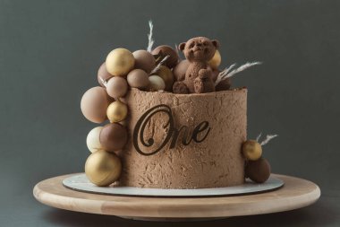 Üzerinde oyuncak ayı olan kahverengi kadife kremalı kek. Koyu yeşil arka planda çikolata kahverengi ve altın küreleri olan küçük bir bebek için doğum günü pastası. Bir yaşında..