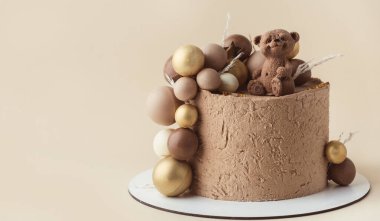 Üzerinde oyuncak ayı olan kahverengi kadife kremalı kek. Bej arka planda çikolata kahverengi ve altın küreleri olan küçük bir bebek için doğum günü pastası. Bir yaşında..