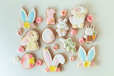 Paskalya tavşanı şeklinde zencefilli kurabiyeler. Beyaz arka planda süslü, şenlikli krema ve çiçeklerle süslenmiş. Düz yatıyordu