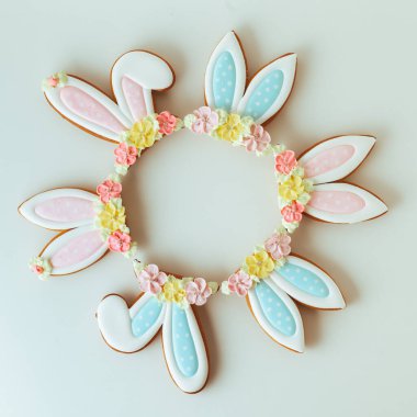 Paskalya tavşanı şeklinde zencefilli kurabiyeler. Beyaz arka planda süslü, şenlikli krema ve çiçeklerle süslenmiş. Düz yatıyordu