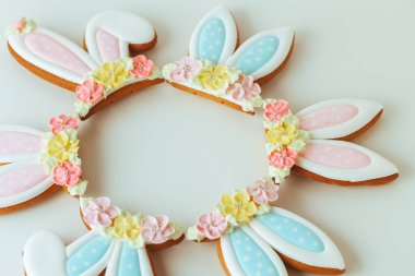 Paskalya tavşanı şeklinde zencefilli kurabiyeler. Beyaz arka planda süslü, şenlikli krema ve çiçeklerle süslenmiş. Düz yatıyordu