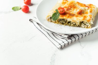 Cannelloni İtalyan makarnası et ve ıspanakla dolu, beyaz arka planda peynirle kaplı.