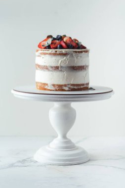 Beyaz arka planda çilek ve yaban mersinli krem peynirli yaz vanilyalı kek. Beyaz pasta standı