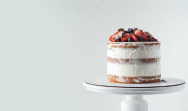 Beyaz arka planda çilek ve yaban mersinli krem peynirli yaz vanilyalı kek. Beyaz pasta standı