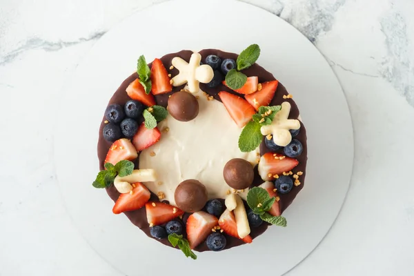 Brown layered cake Three chocolates decorated with bluberries, strawberries and chocolate drips on top. White background. Flat lay