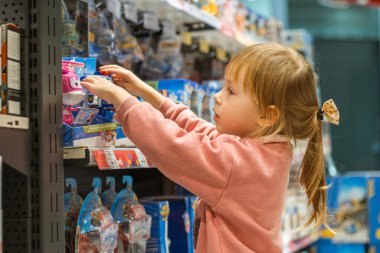 Kyiv, Ukraine - January 29, 2022: Little caucasian girl choosing a new toy in the big baby store. Big shelfs full of toys