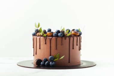 Üzerinde yabanmersini, şeker ve çikolata damlalarıyla süslenmiş kahverengi doğum günü pastası. Beyaz arkaplan.