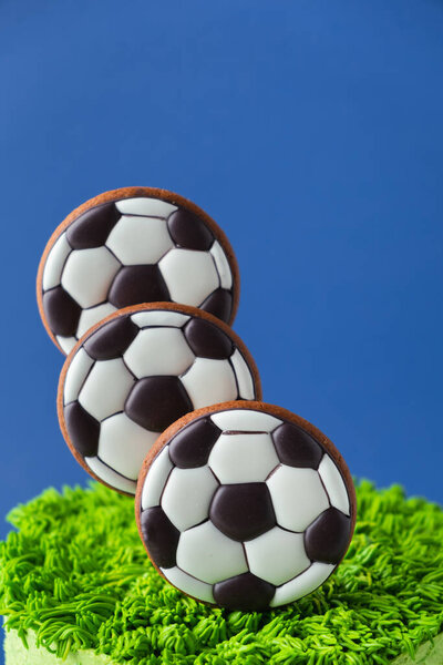 Birthday cake for a football fan with green cream cheese frosting, grass and soccer balls gingerbread cookies on top. Blue background