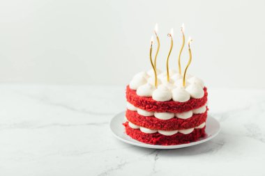 Kırmızı kadife sünger katlı doğum günü pastası ve altın mumlarla süslenmiş beyaz krem peynir.