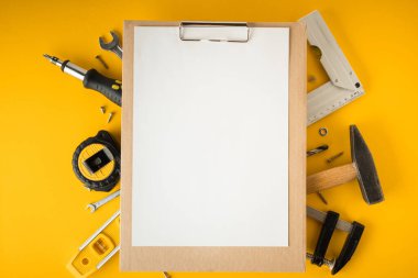 Tamirci aletleri. Kıskaç, anahtar, tornavida, matkap, açı, kabarcık düzeyi ve sarı arka planda mezura. Babalar Günün kutlu olsun. Metnin için içinde boş kağıt olan pano