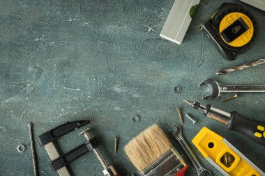 Tamirci aletleri. Kıskaç, İngiliz anahtarı, tornavida, matkap, açı, kabarcık seviyesi ve gri beton arka planda mezura. Babalar Günün kutlu olsun. Metin için boş alan