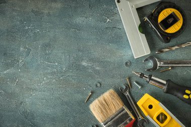 Tamirci aletleri. Kıskaç, İngiliz anahtarı, tornavida, matkap, açı, kabarcık seviyesi ve gri beton arka planda mezura. Babalar Günün kutlu olsun. Metin için boş alan