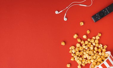 Kırmızı arka planda uzaktan kumandalı ve kulaklıklı kırmızı ve beyaz bir kovadan yayılmış karamelli patlamış mısır. Düz yatıyordu. Kopya alanı ile sinema reklamları