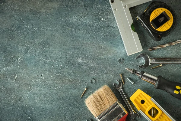 Tamirci aletleri. Kıskaç, İngiliz anahtarı, tornavida, matkap, açı, kabarcık seviyesi ve gri beton arka planda mezura. Babalar Günün kutlu olsun. Metin için boş alan