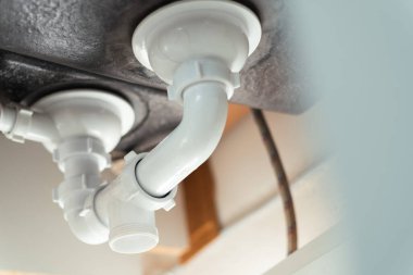 Kanalizasyon ve lavabo sifonunu yakın çekim. Tesisatçı lavabo giderlerini tamir ediyor.