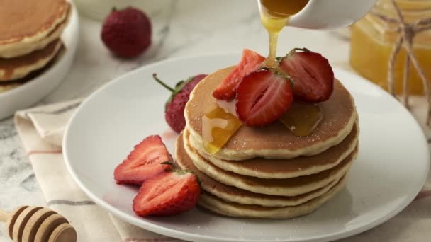将糖浆或蜂蜜倒在装饰有草莓的美国煎饼上 美味而健康的早餐 — 图库视频影像