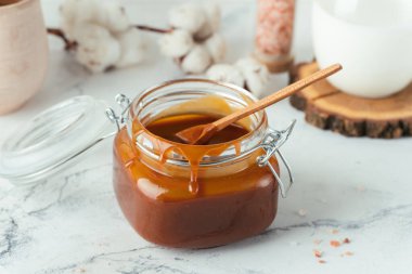 Cam kavanoz kahverengi tuzlu karamel, içinde leke ve ahşap kaşık var.