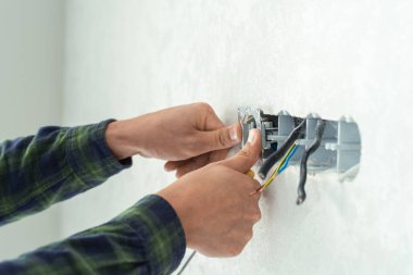 Elektrikçi beyaz bir duvara yeni bir soket takıyor. Yeni bir dairede yenileme işlemi