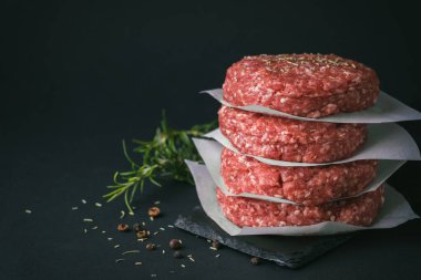 Çiğ kıymalı burger köfteleri, siyah arka planda pişen kağıtlarla ayrılır.