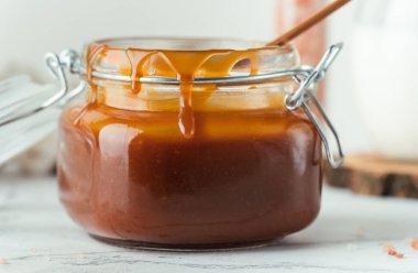 Cam kavanoz kahverengi tuzlu karamel, içinde leke ve ahşap kaşık var.