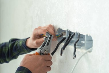 Elektrikçi beyaz bir duvara yeni bir soket takıyor. Yeni bir dairede yenileme işlemi