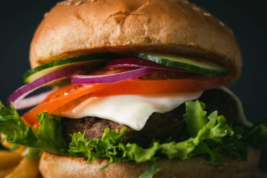 Büyük köfteli burger, peynirli, mor, soğanlı, salatalıklı, patates kızartmalı, ahşap, siyah, siyah arka planda.