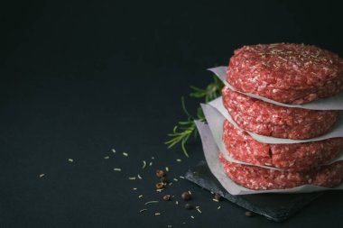 Siyah arka planda parşömen kağıdıyla ayrılmış çiğ et köfteleri.