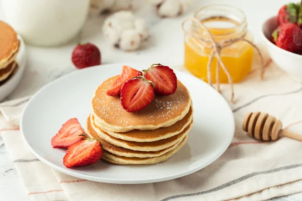 American pancakes decorated with strawberries and sprinkled with powdered sugar in a white plate. Healthy and tasty breakfast