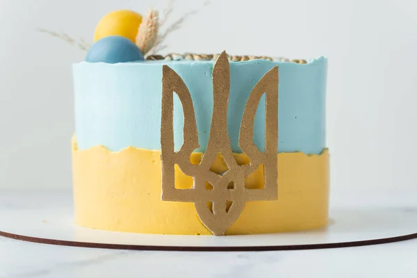 Patriotic cake with yellow and blue cream cheese frosting decorated with the state coat of arms of Ukraine. Independence Day Cake. Cake for the defender of Ukraine