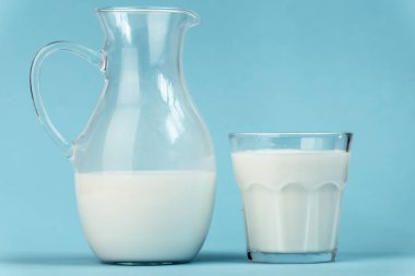 Mavi arka planda sürahi ve bardak dolusu süt. Süt ürünleri konseptinin faydaları