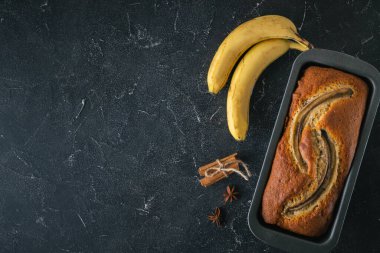 Siyah bir yemek kabında taze muzların yanında siyah beton bir arka planda taze muzlu turta. Ev yapımı hamur işi konsepti. Düz yatıyordu. Boşluğu kopyala