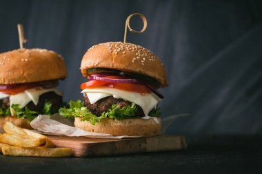 Büyük köfteli burger, peynirli, mor, soğanlı, salatalıklı, patates kızartmalı, ahşap, siyah, siyah arka planda.