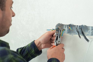 Elektrikçi beyaz bir duvara yeni bir soket takıyor. Yeni bir dairede yenileme işlemi