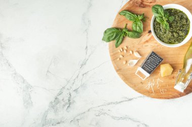 Beyaz kasede pesto sosu için gerekli malzemeler. Yeşil fesleğen yaprağı, parmesan peyniri ve ahşap arka planda çam fıstığı. Düz yatıyordu. Genel Görünüm