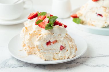 Dilimlenmiş çilekle süslenmiş pudra şekerli krema rulosu beyaz arka planda beyaz tabakta servis edilir. Makro çekim