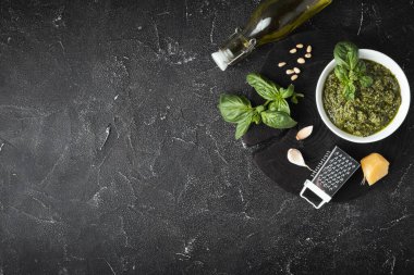 Beyaz kasede pesto sosu için gerekli malzemeler. Siyah arka planda yeşil fesleğen yaprağı, parmesan peyniri ve çam fıstığı. Düz yatıyordu. Genel Görünüm