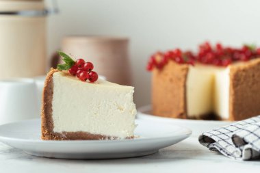 Beyaz tabaktaki klasik New York peynirli keki beyaz arka planda kırmızı frenk üzümü ile süslenmiş.